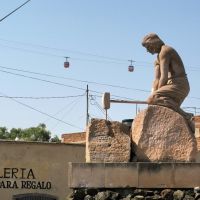Two cablecars are crossing behind a statue of a worker with a hammer, Сомбререт