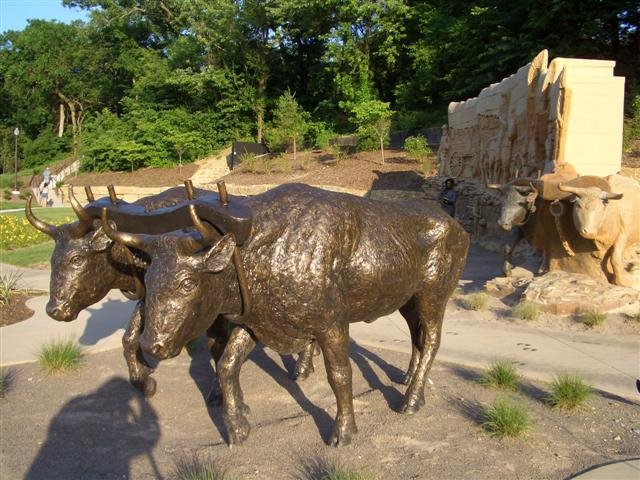 wagon train, life-size, clay/stone facade, clay/stone/bronze oxen, bronze oxen, and bronze woman with child, Pioneer Crossing Park,Shawnee,KS, Мерриам
