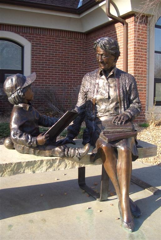 Sharing Art Through Sculpture, life size bronze on stone bench on south side of Coffee County Library - Burlington Branch, Burlington, KS, Овербрук