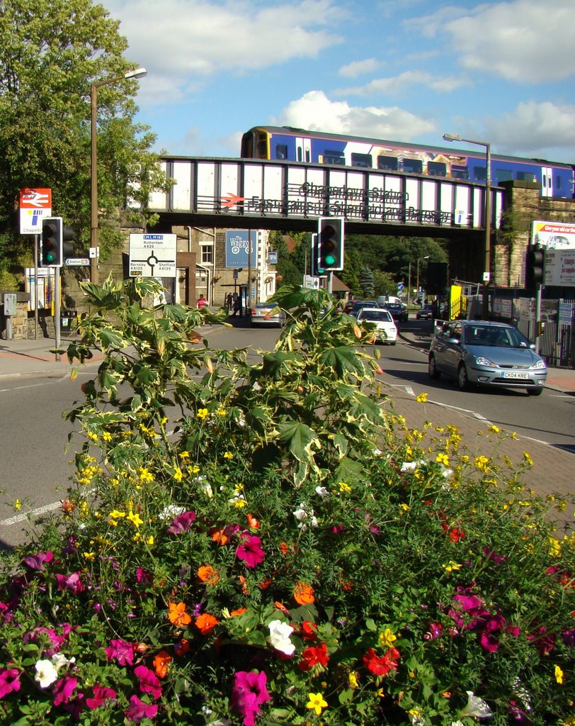Looking over flower display towards train on the bridge leaving Chapeltown Station, Sheffield S35, Чапелтаун